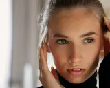 Primo piano di una giovane donna con lentiggini, che si tocca il viso. Il suo sguardo intenso e le sopracciglia leggermente alzate suggeriscono sorpresa o curiosità, rivelando il significato psicologico di questo gesto.