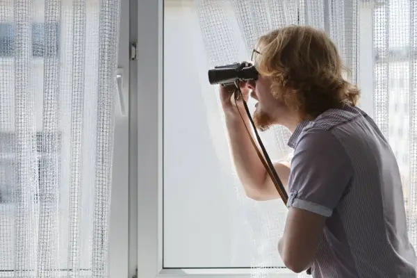 Uomo con binocolo spia dalla finestra, forse per atti persecutori vicino di casa.